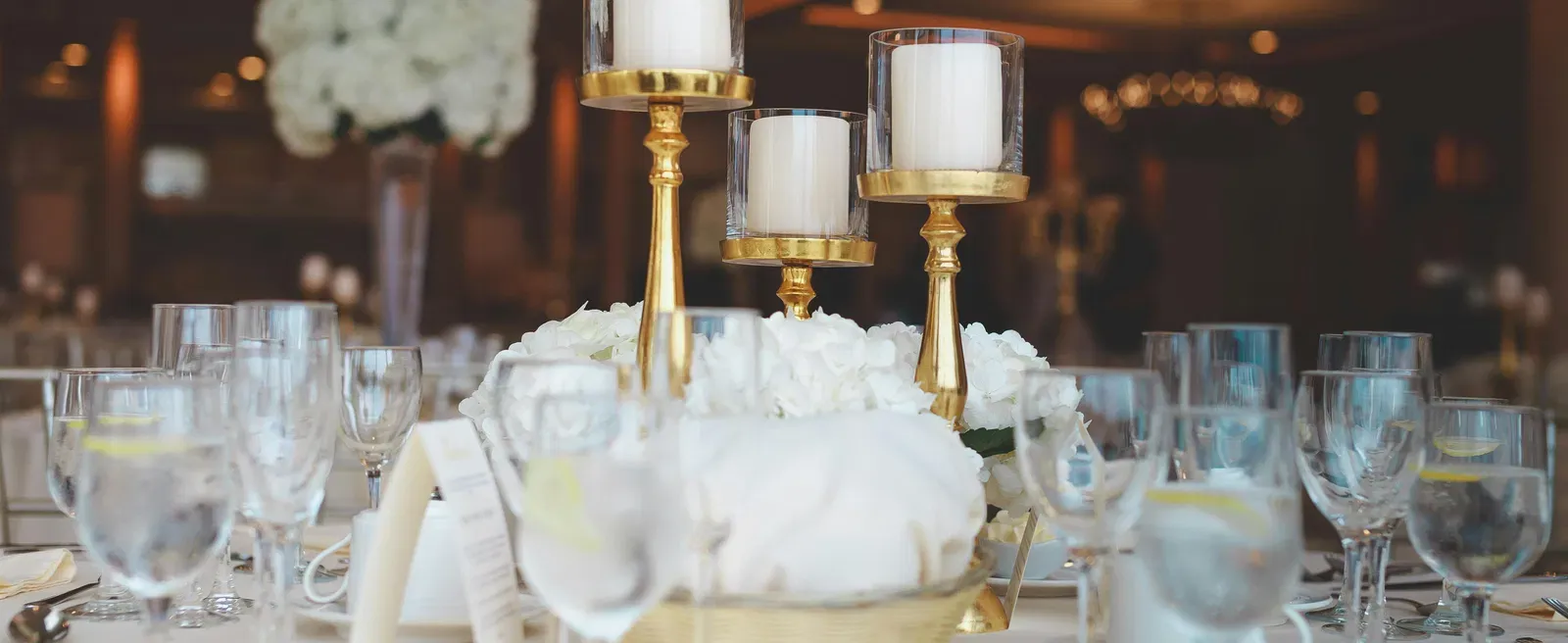 Selective focus photography of a centre table decorated with candles and wine glasses on a white cloth.