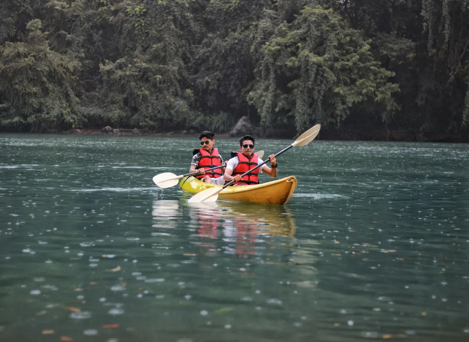 Two men kayaking on a lake surrounded by a forest.